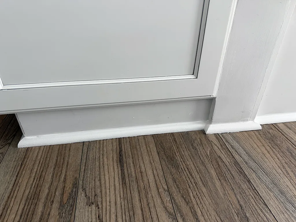 Finished white baseboard and door casing meeting wood flooring in a clean line