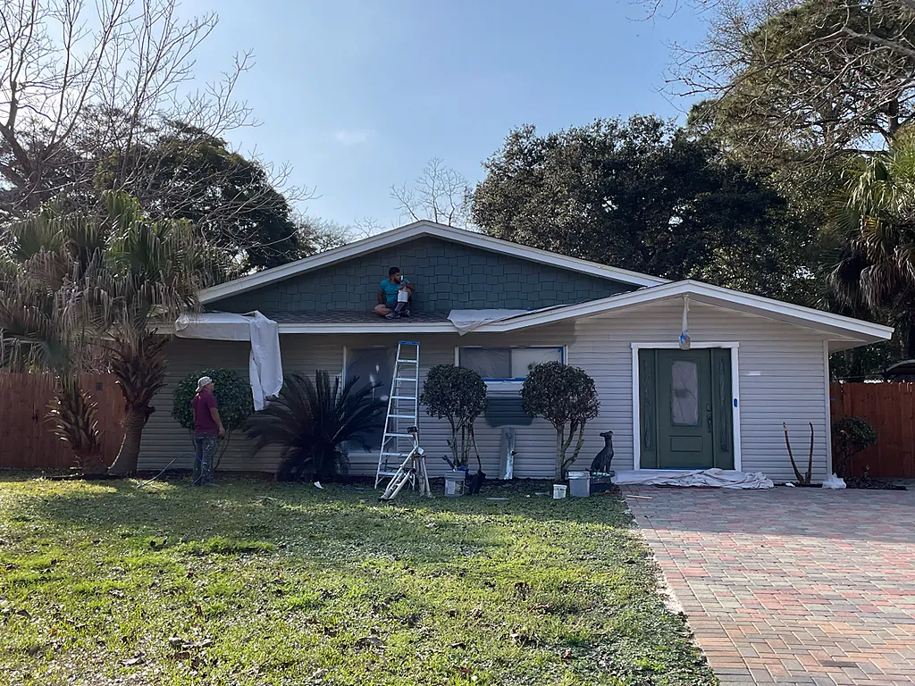 Painters masking and cutting in the gable of a Destin, Florida home partway through an exterior repaint