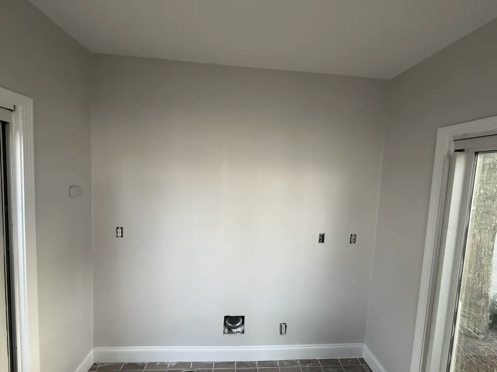 The same wall made smooth and painted light gray, with white baseboard and door trim