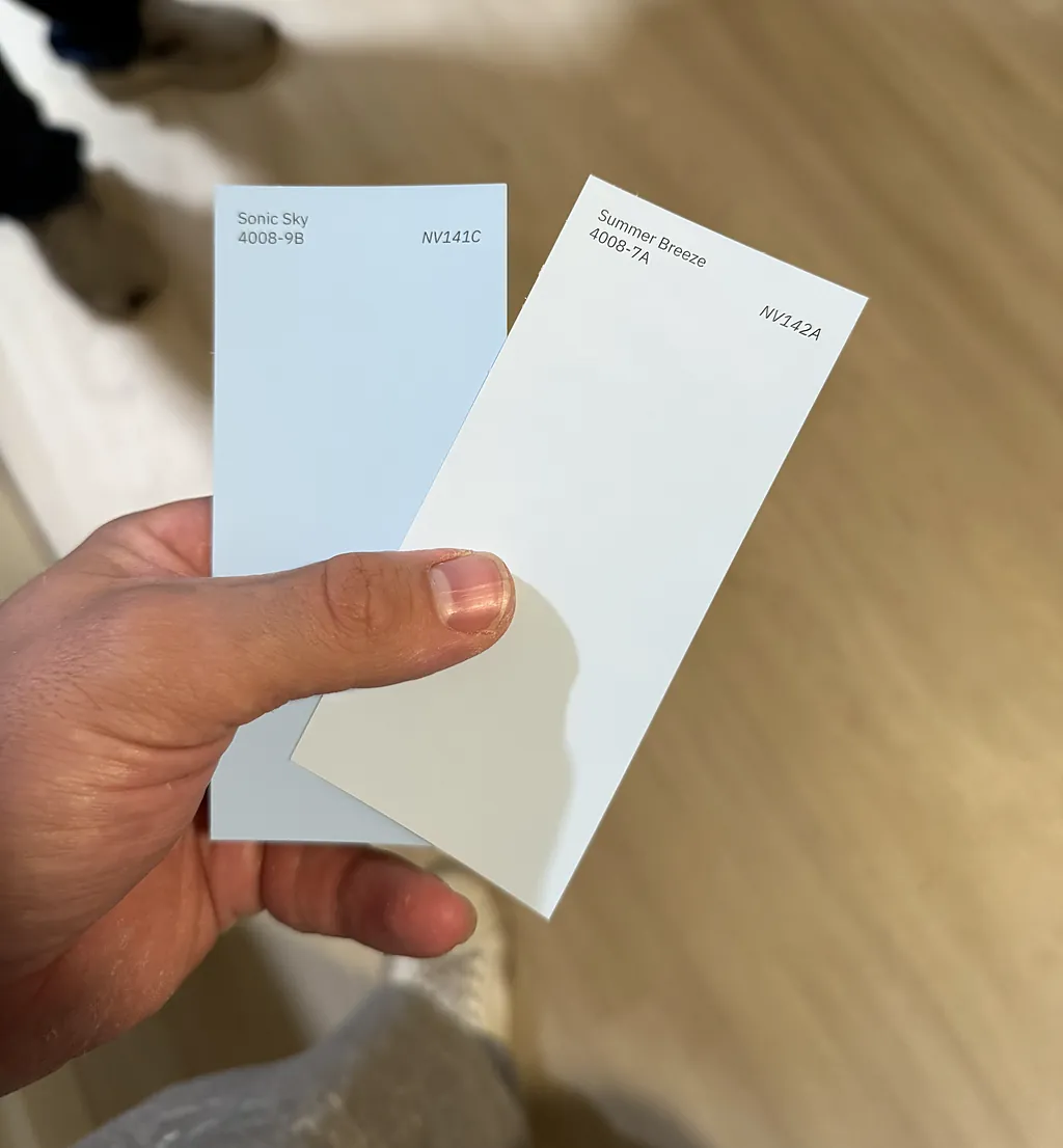 Two soft white and gray paint swatches held up on site while choosing colors