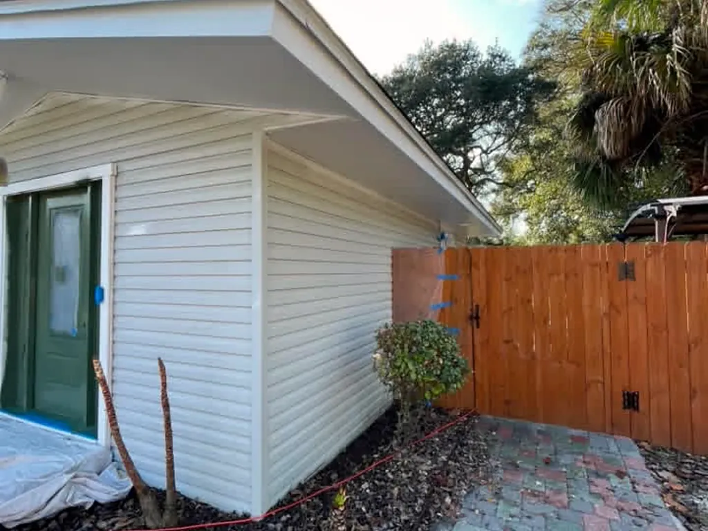 Cream vinyl siding and a side entry door masked off and prepared for painting at a Destin, Florida home